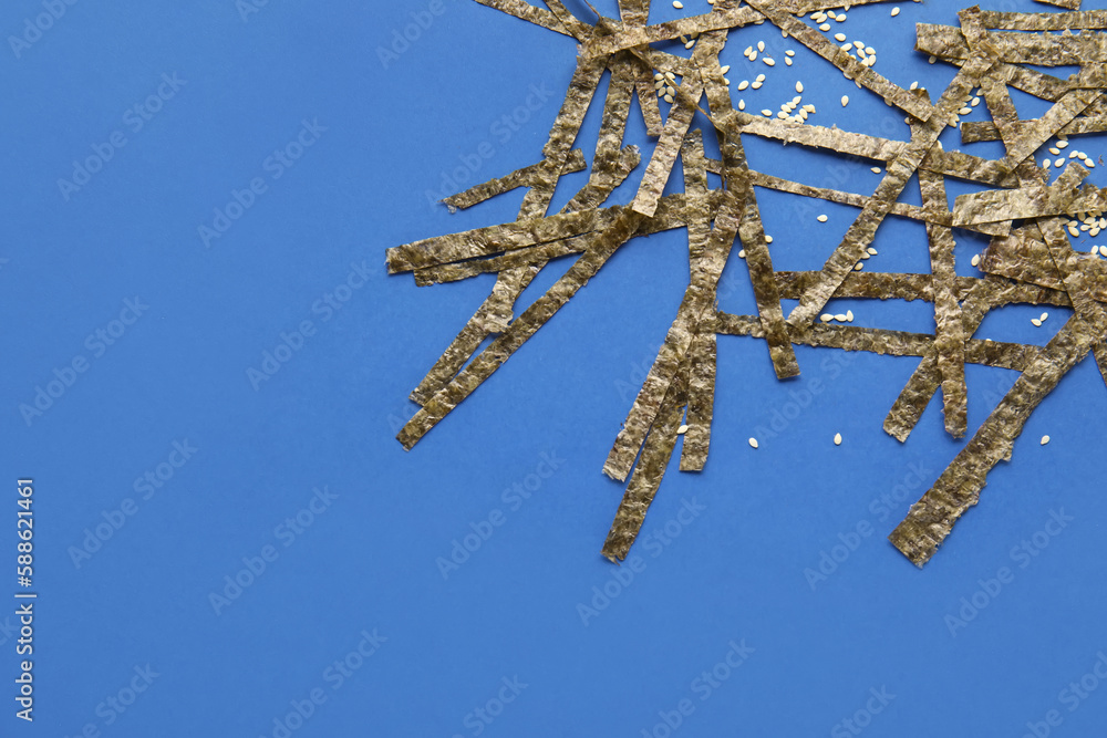 Cut nori sheets and sesame seeds on blue background