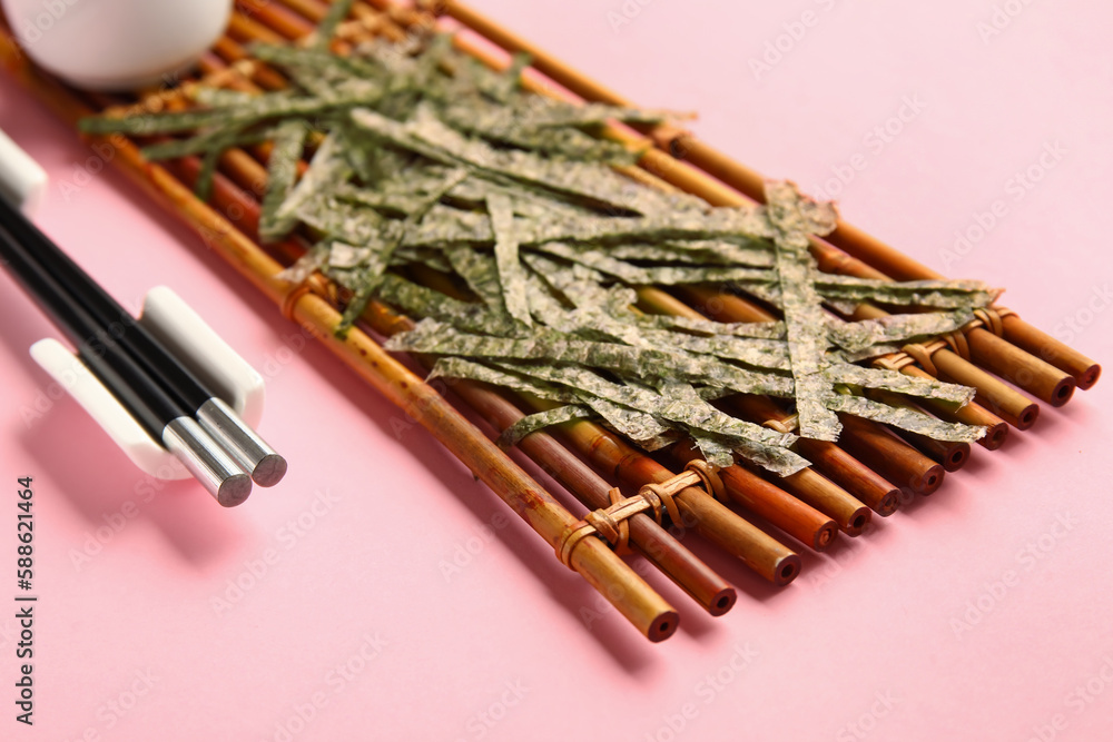 Bamboo mat with cut nori sheets on pink background, closeup