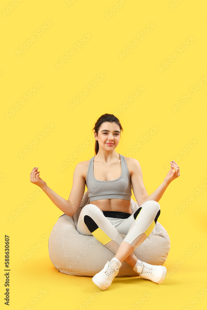 Sporty young woman meditating on yellow background