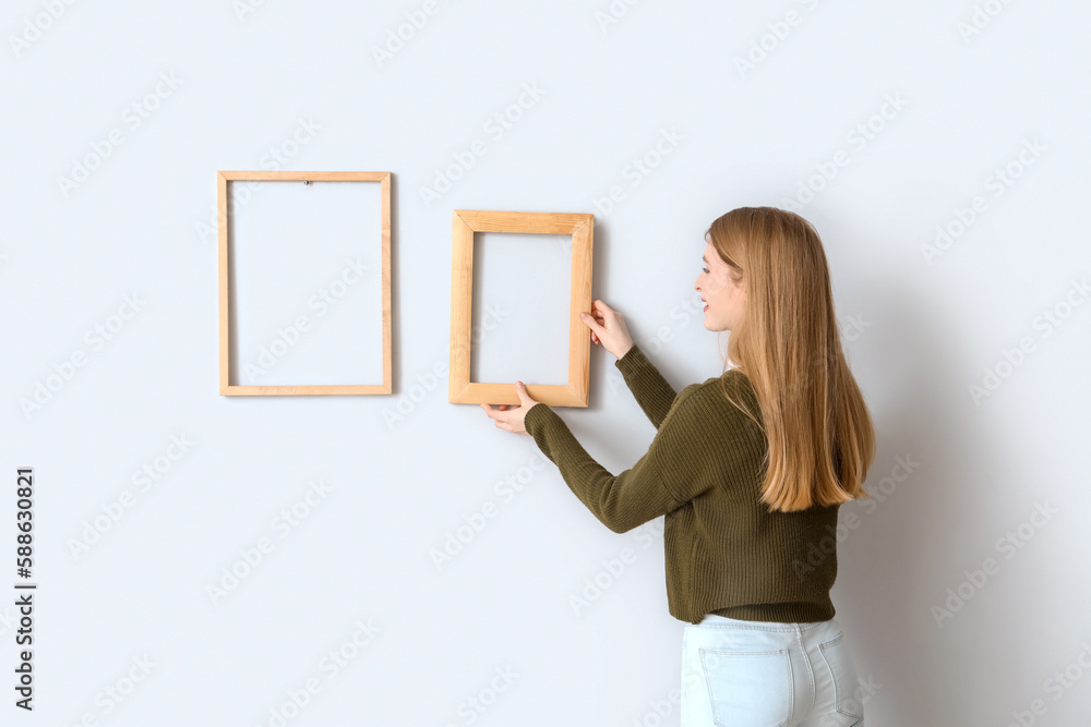 Young woman hanging frame on light wall