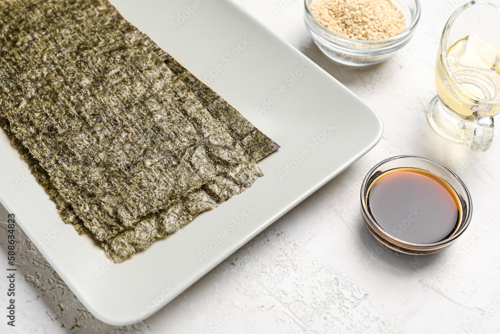 Plate with nori sheets, soy sauce, sesame seeds and vinegar on light background, closeup