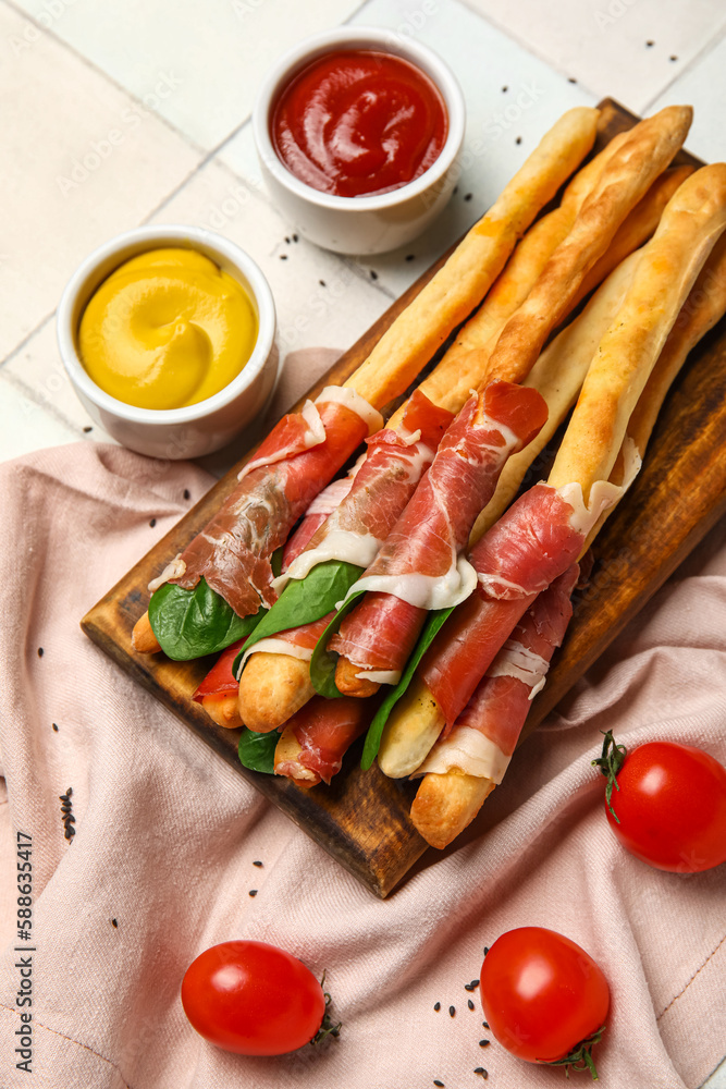 Wooden board of tasty Italian Grissini with bacon on white tile background