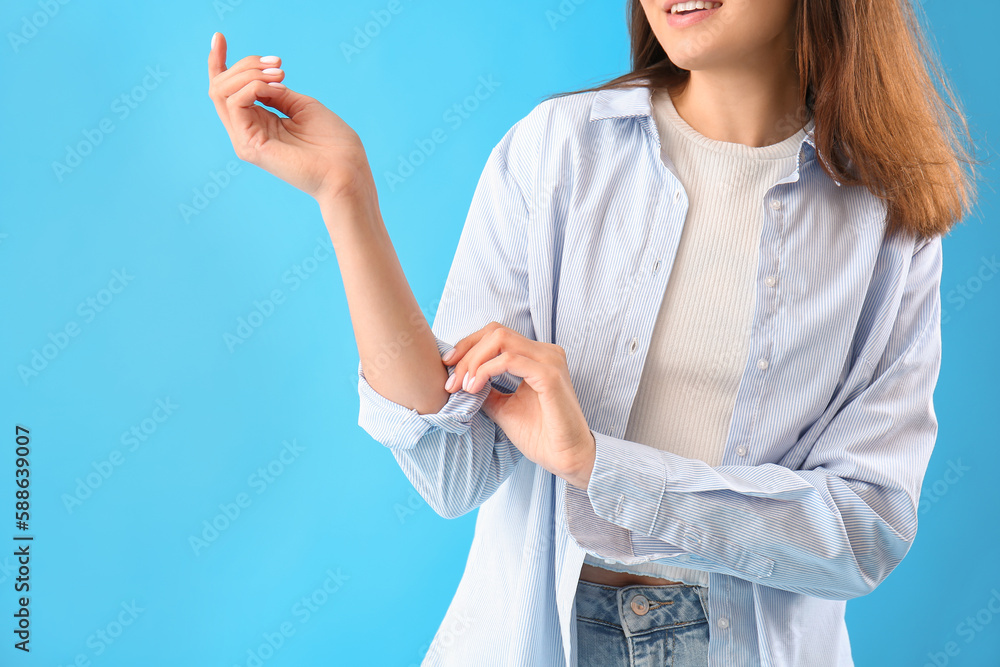 Young woman rolling up her sleeve on light blue background