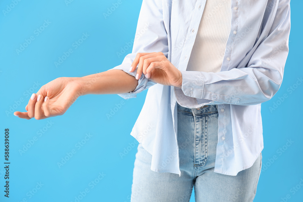 Young woman rolling up her sleeve on light blue background