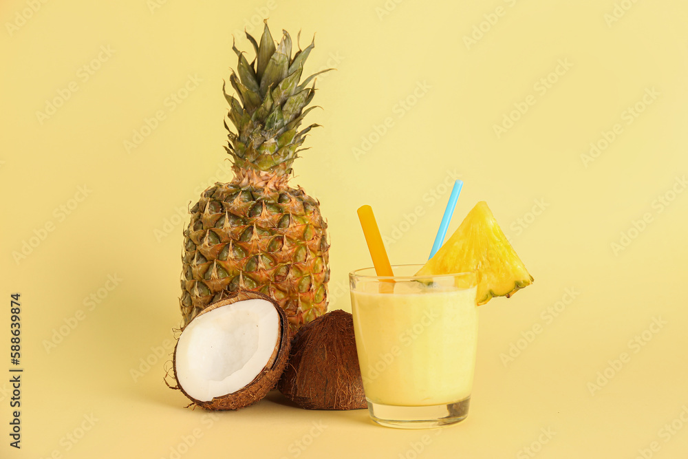 Glass of tasty pineapple smoothie, straw and coconut on yellow background