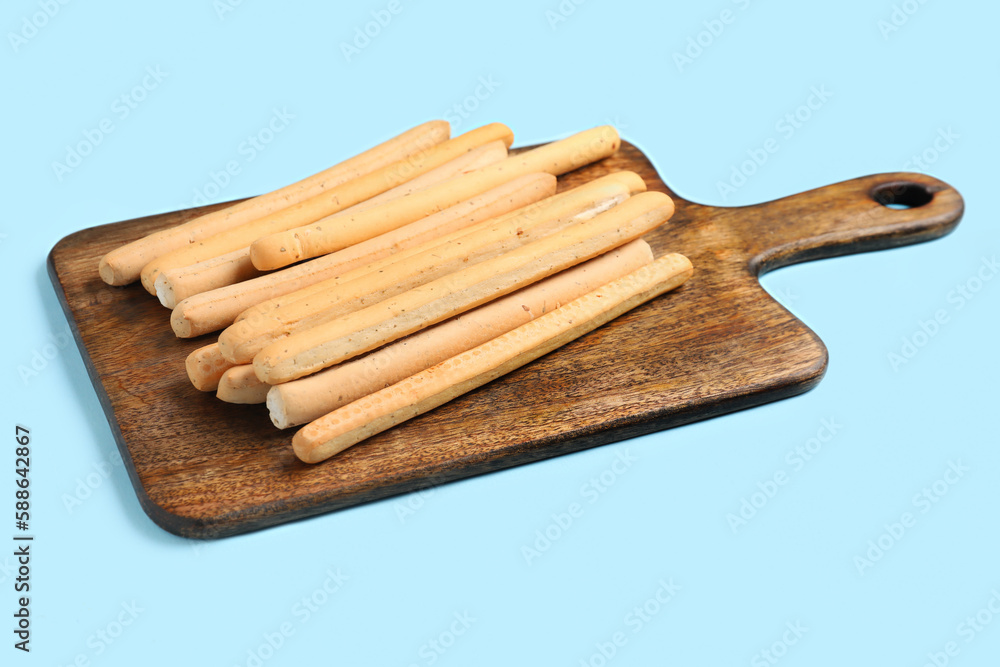 Wooden board with tasty Italian Grissini on blue background