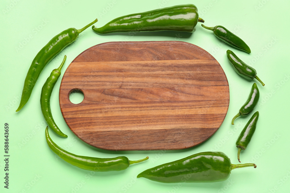 Composition with green peppers and wooden board on color background