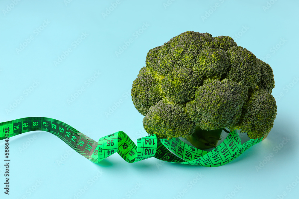 Broccoli and green measuring tape on blue background. Diet concept