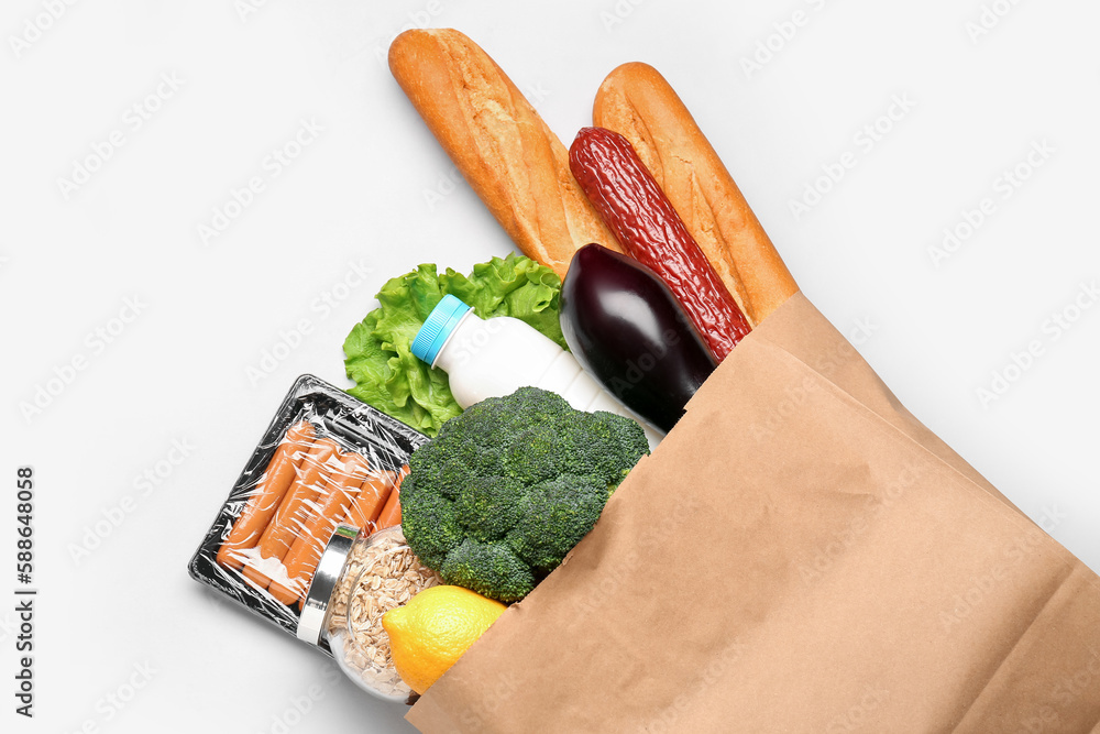 Paper bag with vegetables, cereal, bread and milk on grey background