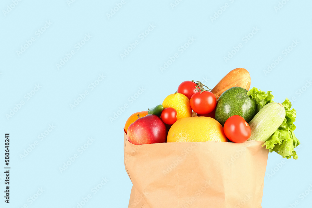 Paper bag with vegetables and fruits on light blue background