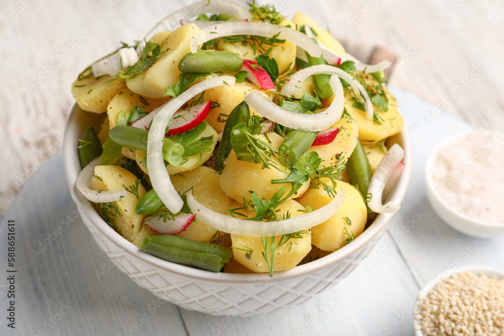 Bowl of tasty Potato Salad with vegetables on light wooden background, closeup