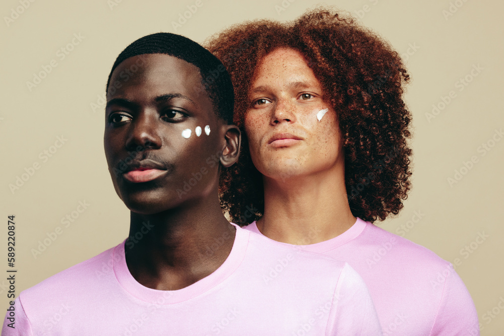 Two young men with unique skin tones use beauty cream on their faces