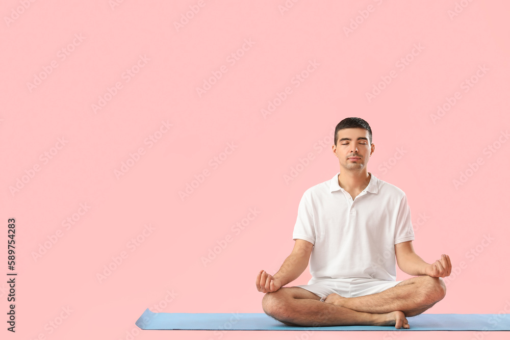 Young man meditating on pink background