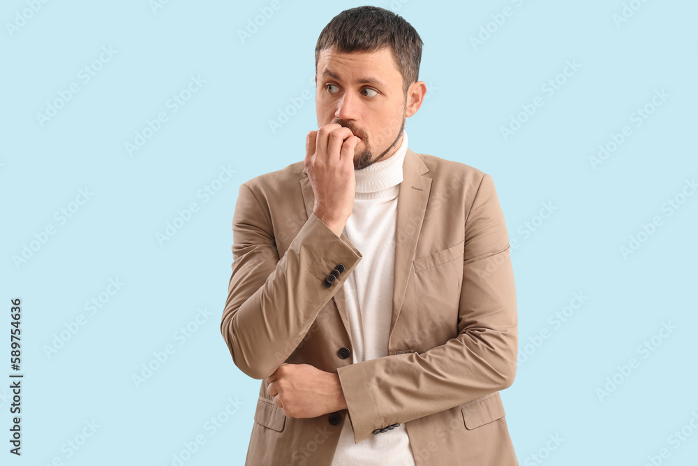 Handsome businessman biting nails on blue background