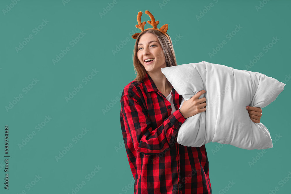 Young woman in reindeer horns with pillow on green background