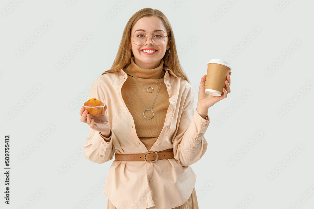 Young woman with tasty cupcake and cup of coffee on light background