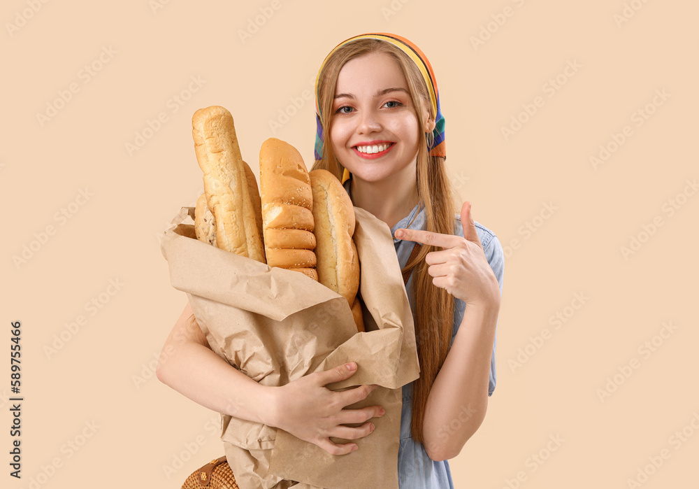 Young woman pointing at fresh baguettes on beige background