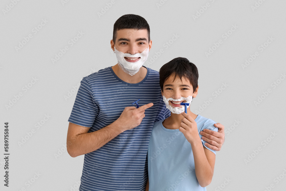 Father and his little son shaving against light background