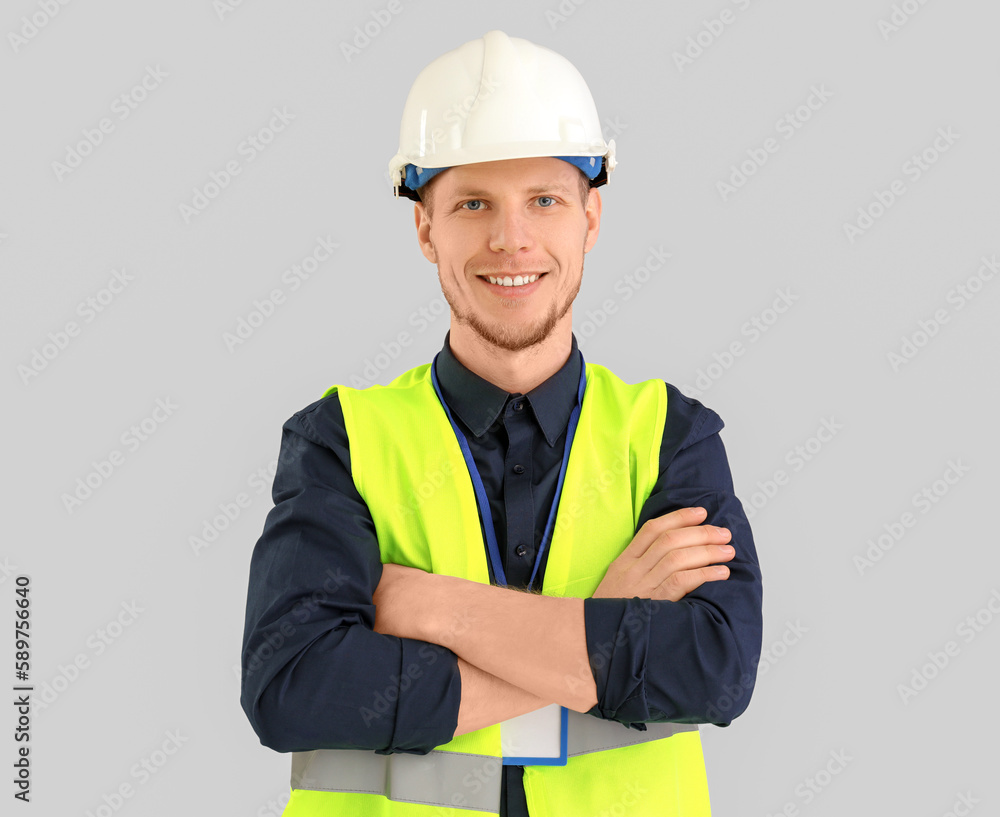 Male worker in vest and hardhat on grey background