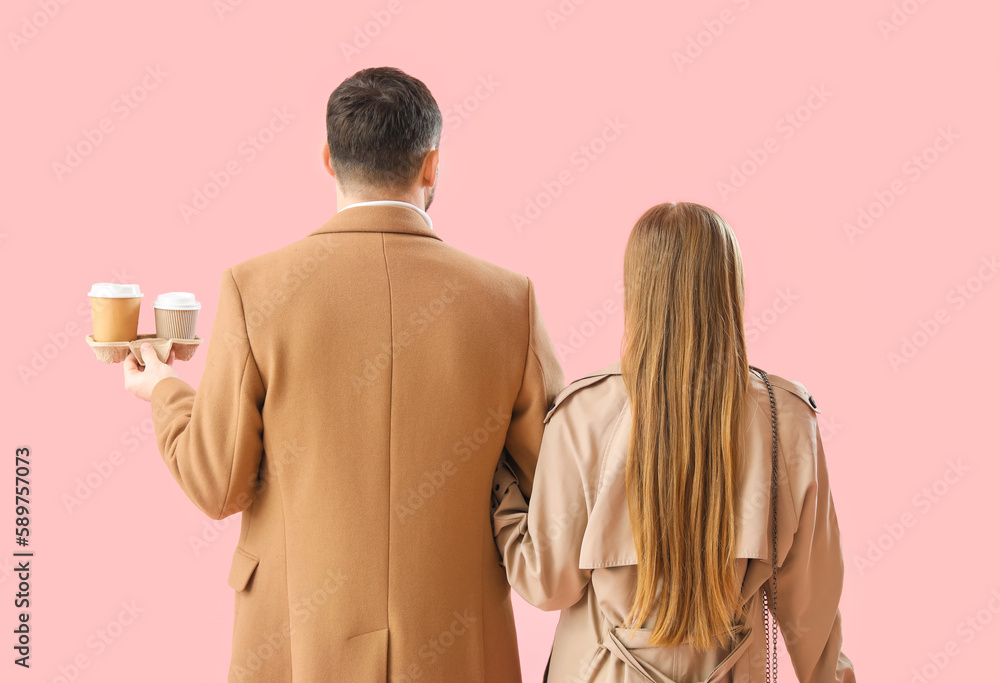 Young couple with cups of coffee on pink background, back view