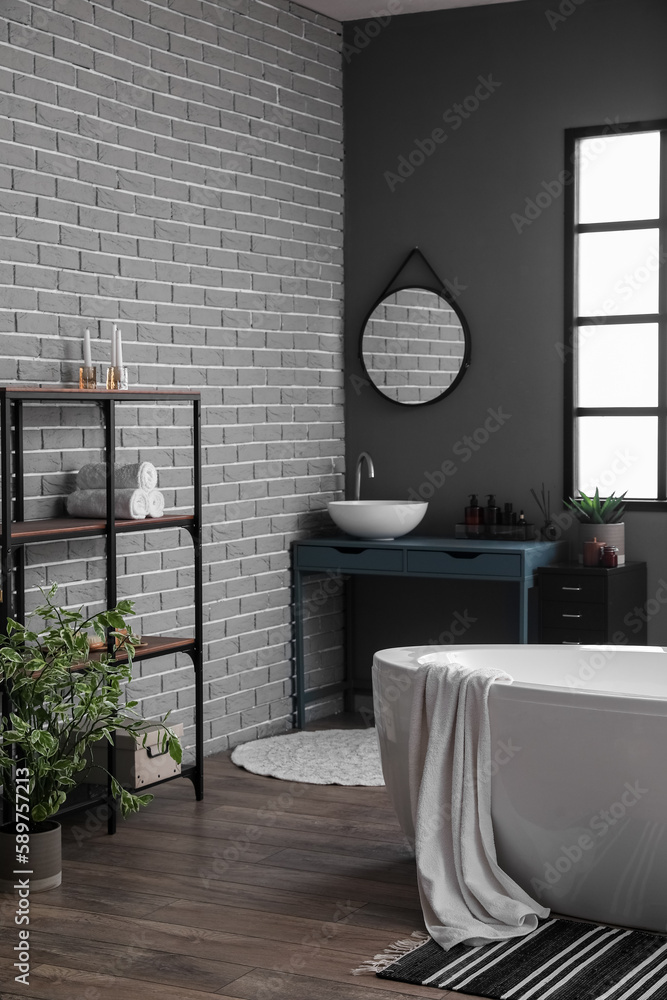 Interior of modern bathroom with bathtub, sink and shelving unit