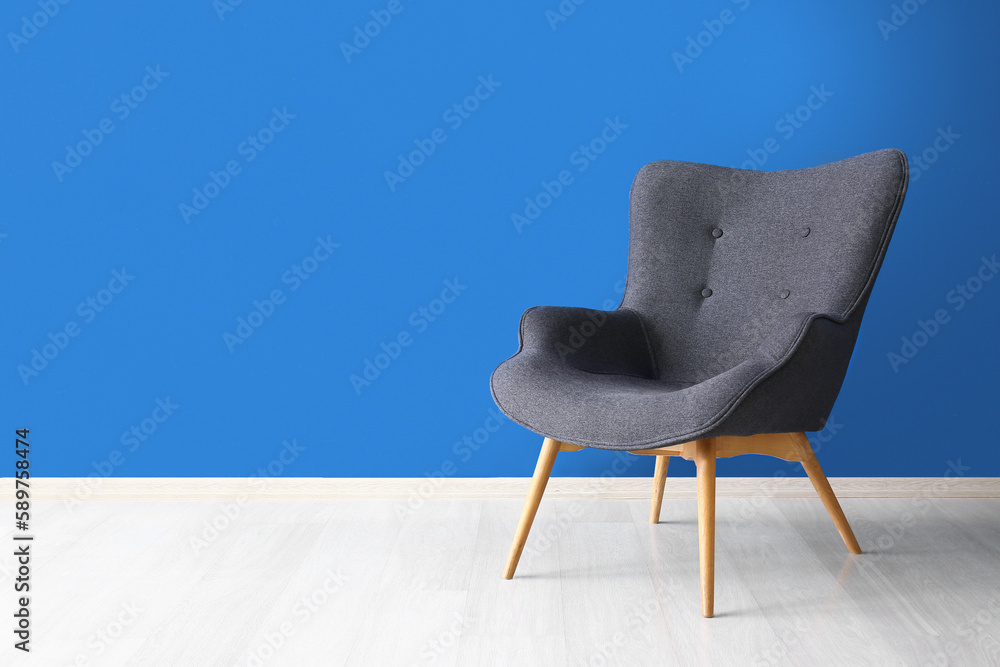 Stylish grey armchair near blue wall