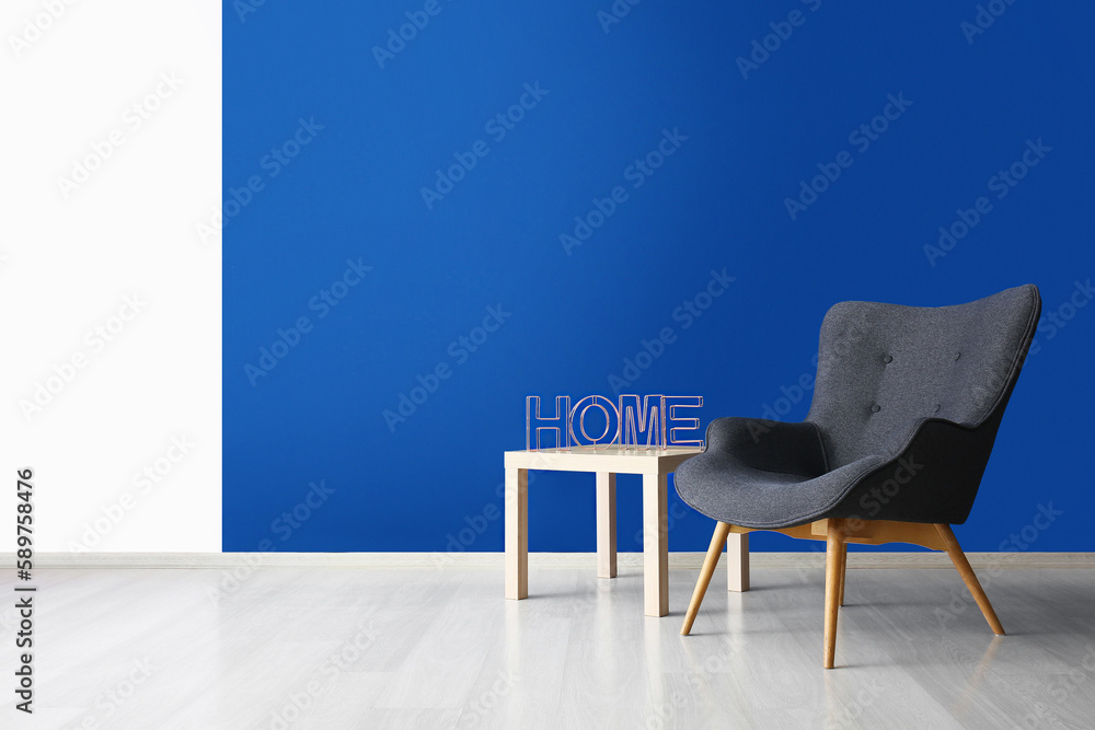 Stylish grey armchair and word HOME on table near blue wall