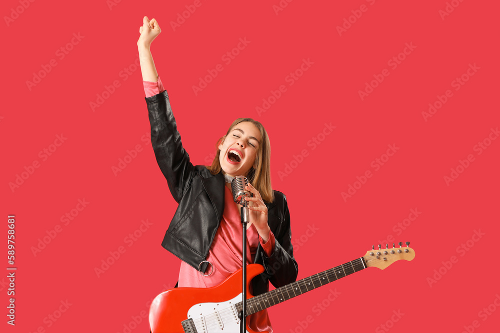 Young woman with guitar and microphone singing on red background