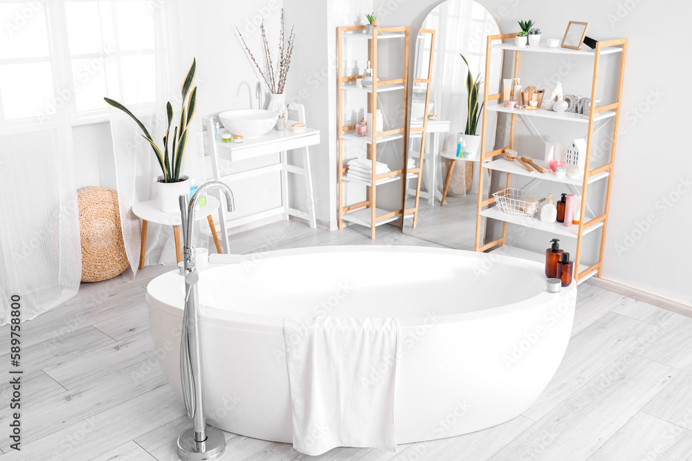 Interior of bathroom with bathtub, mirror and shelving units