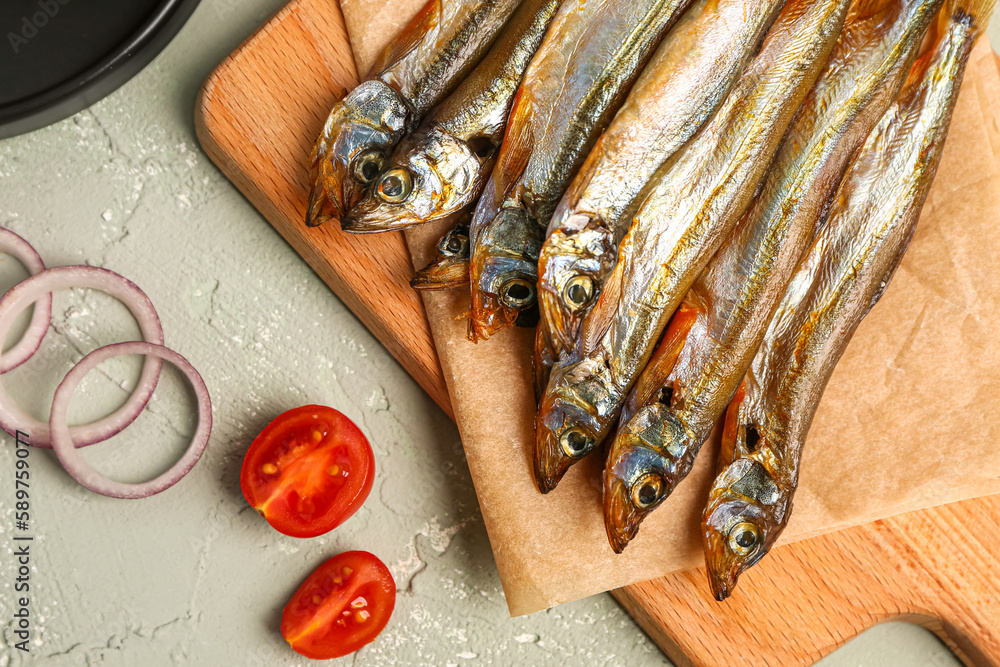 Board with tasty smoked capelin on grey background