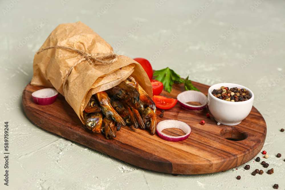 Board with tasty smoked capelin wrapped in parchment on grey background