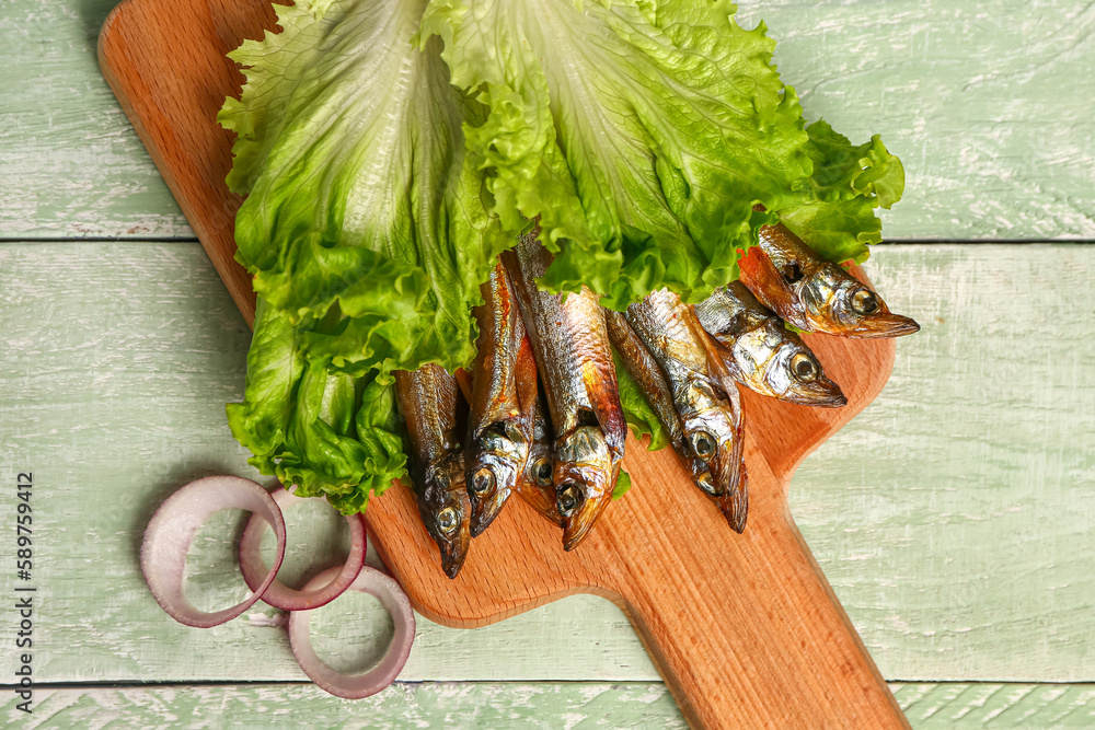 Board with tasty smoked capelin wrapped in lettuce on green wooden background