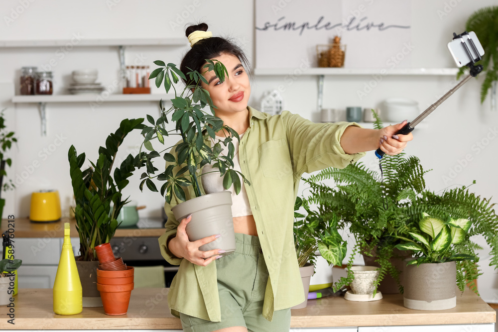 Young woman with green houseplants taking selfie in kitchen