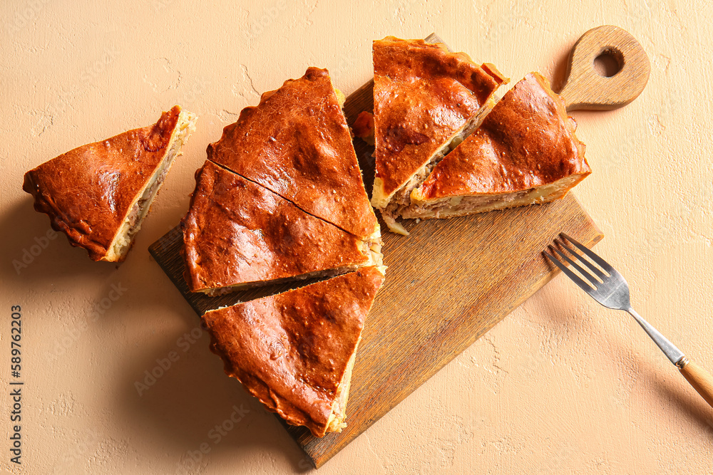 Board with pieces of delicious meat pie and fork on beige table