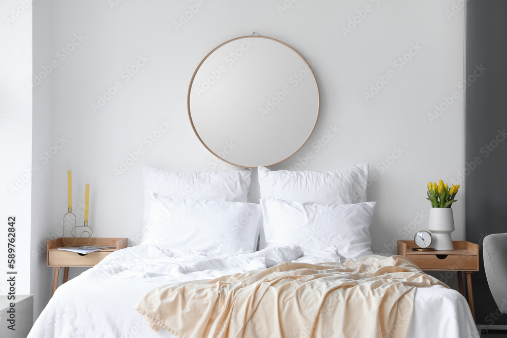 Interior of light bedroom with mirror and tulips in vase