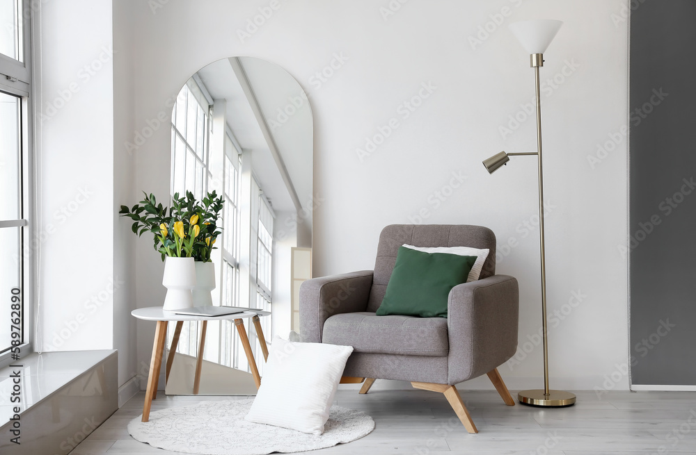 Interior of living room with mirror, armchair and tulips in vase