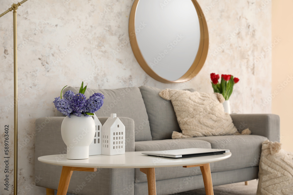 Vase with flowers, candle holders and laptop on table in living room