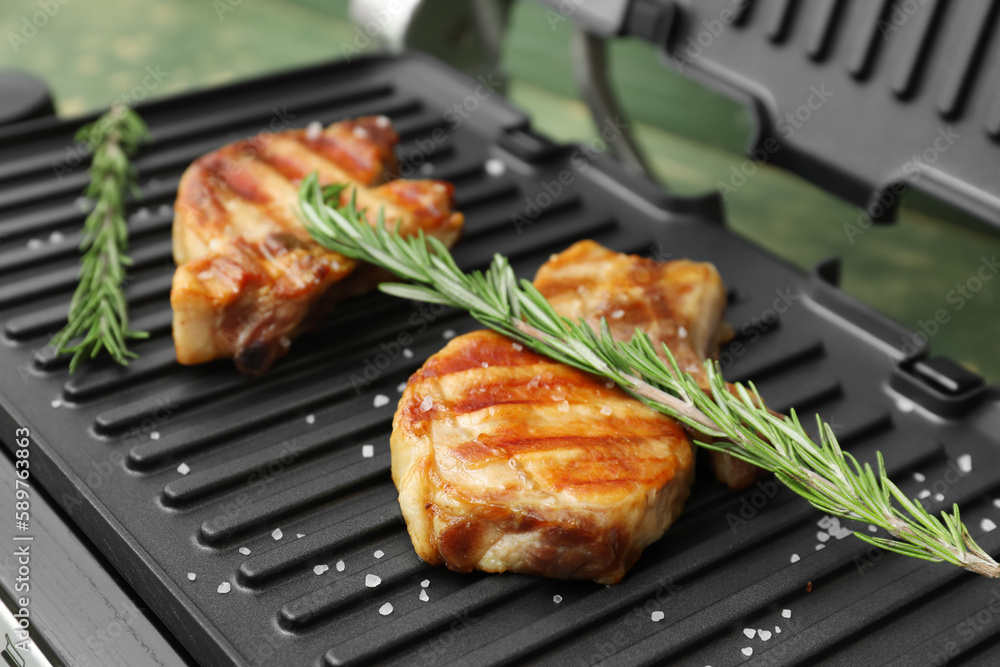 Delicious steaks and rosemary on modern electric grill, closeup