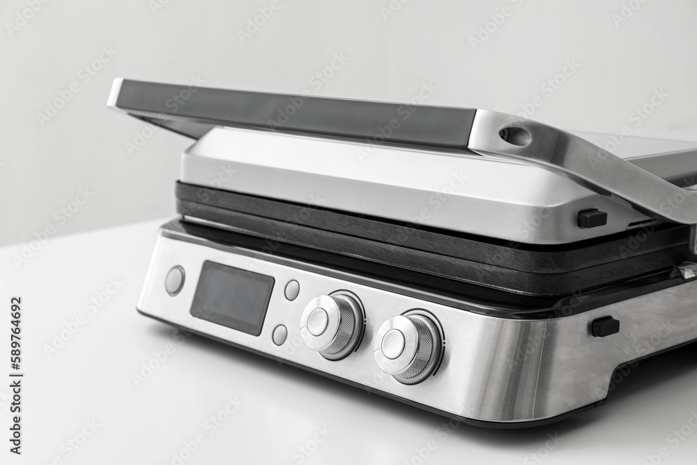 Modern electric grill with closed lid on white table against grey background, closeup