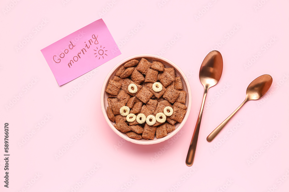 Bowl of tasty corn pillows, spoons and paper with text GOOD MORNING on pink background