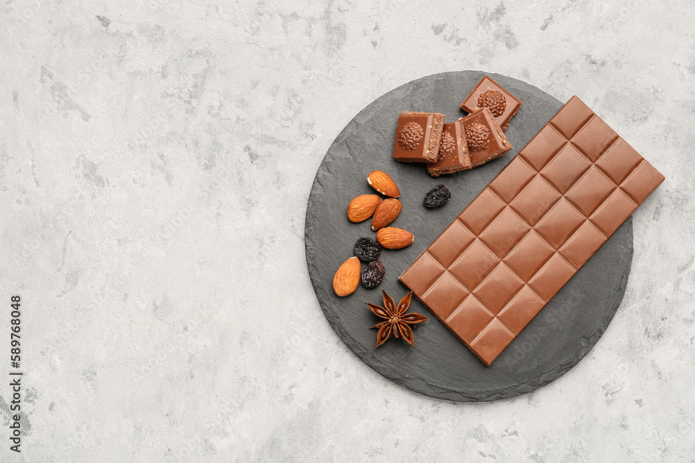 Slate board with tasty chocolate, almonds, raisins and anise on light background