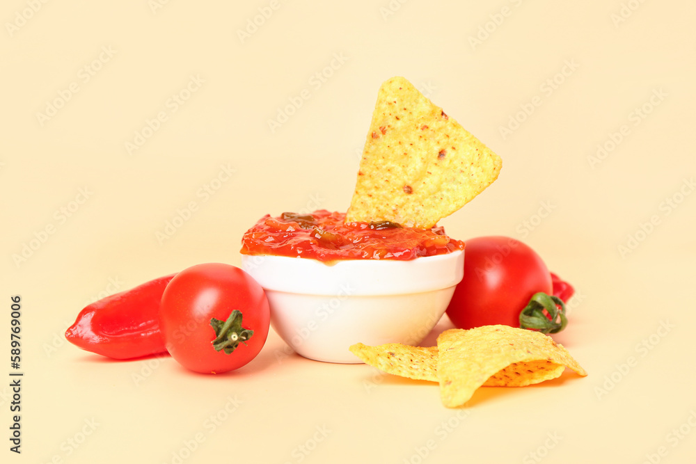 Bowl of tasty salsa sauce, vegetables and nachos on color background