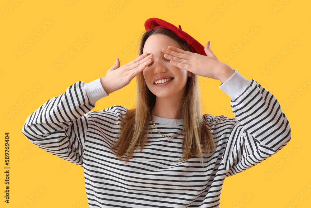 Young woman closing her eyes with hands on yellow background