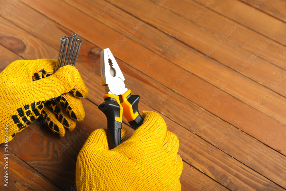 Male hands in gloves holding pliers and nails on wooden background