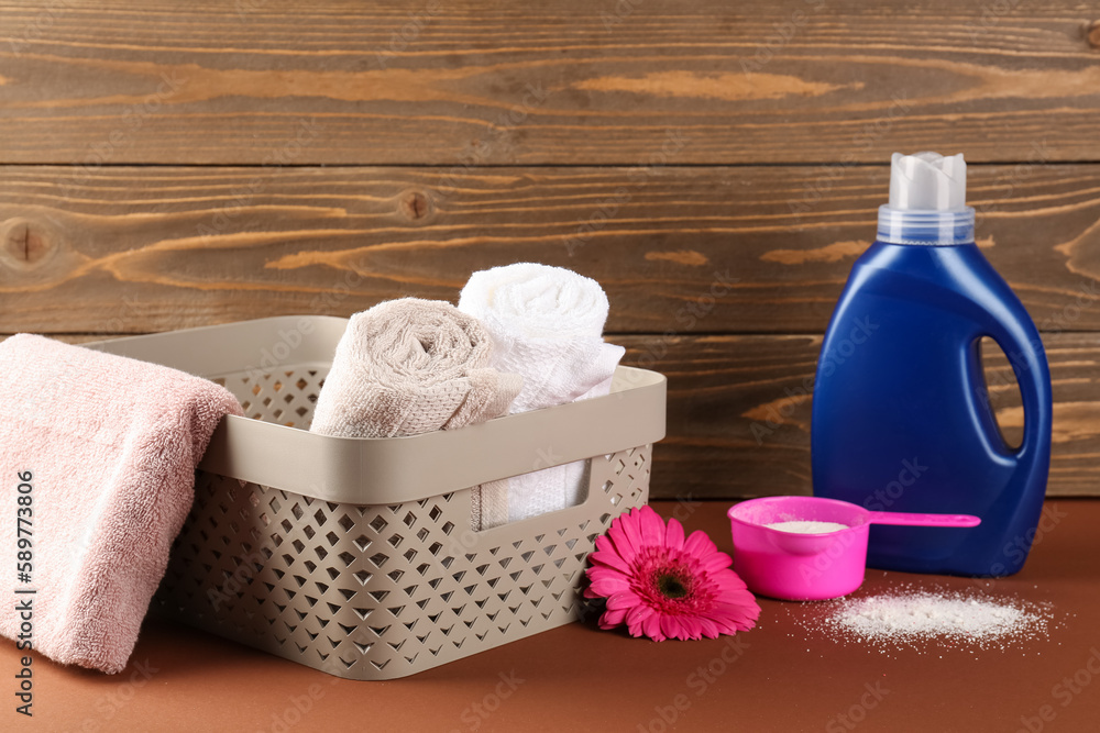 Laundry detergents, gerbera flower and basket with towels on brown table against wooden background