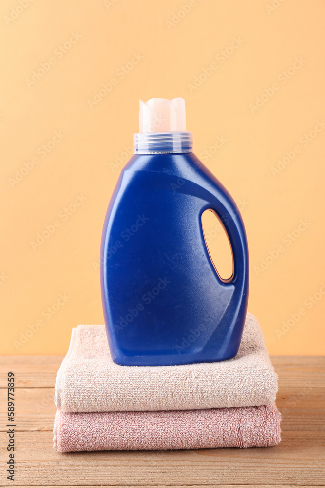 Laundry detergent and folded towels on wooden table against orange background