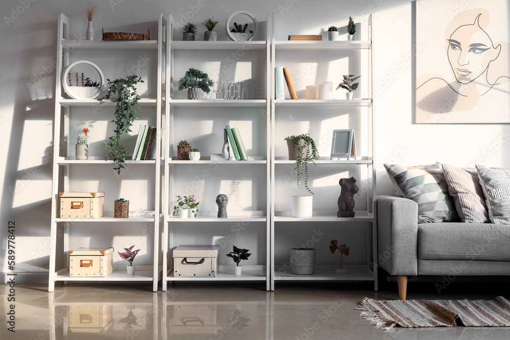 Interior of light living room with sofa, shelving units and artificial plants