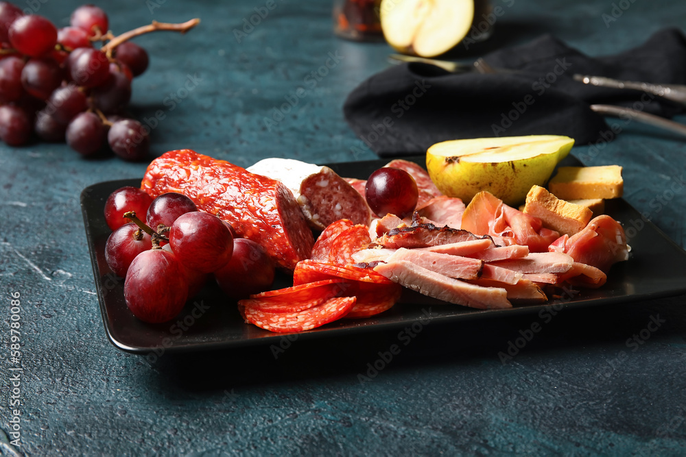 Plate with assortment of tasty deli meats on black background