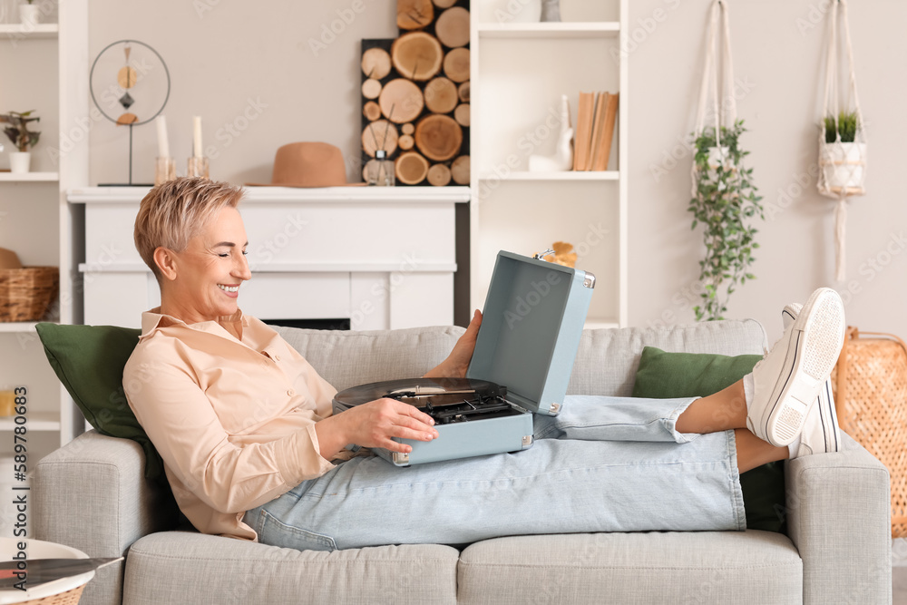 Mature woman with record player lying on sofa at home