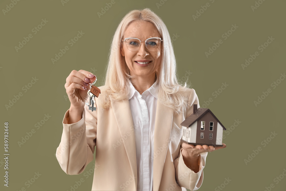 Mature real estate agent with keys and house model on green background